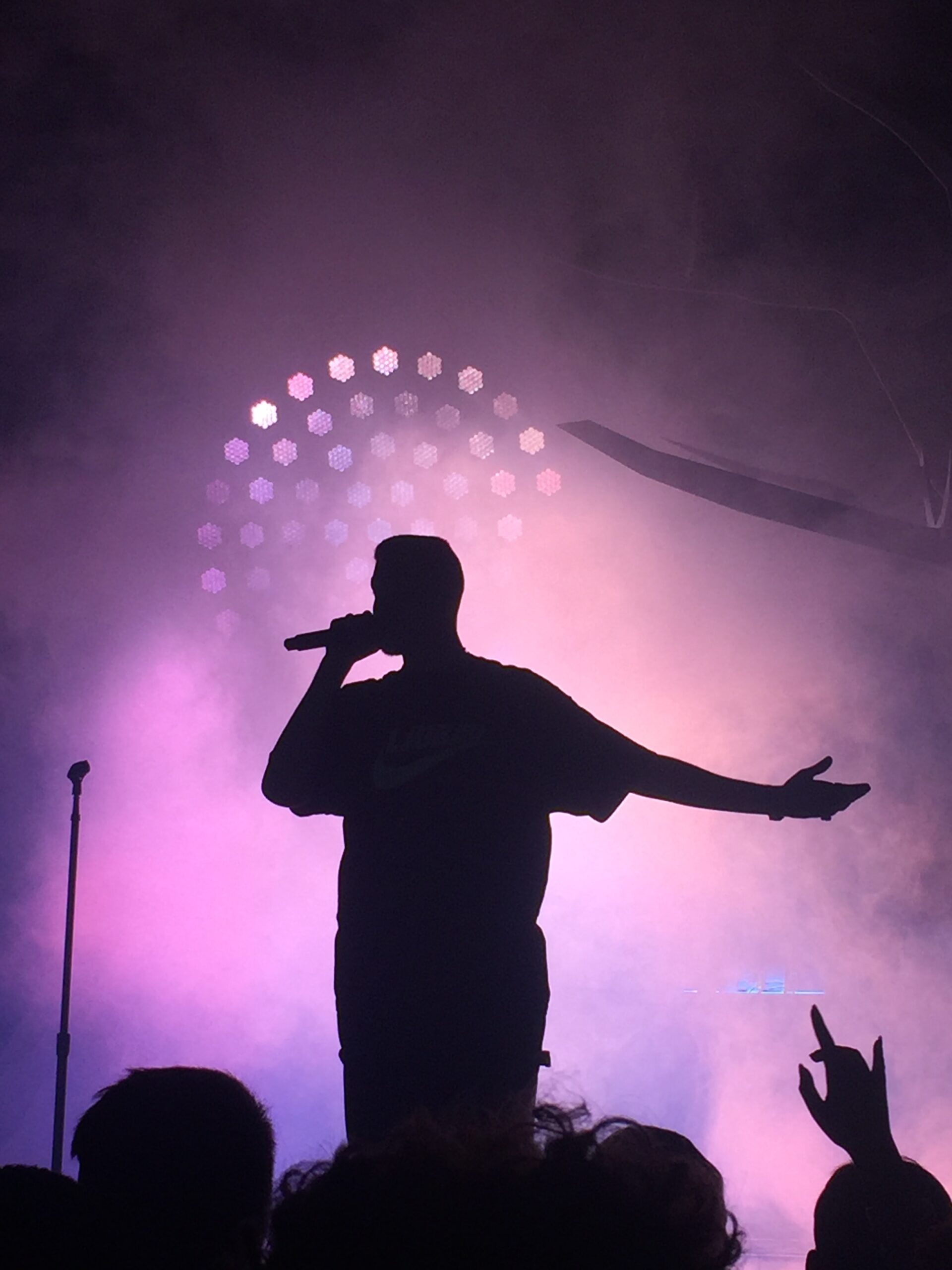 A man is singing on stage with purple lights in the background.